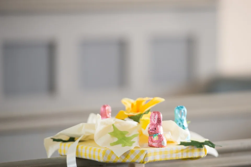 a table in a church with chocolate rabbits in pink and blue foil and fake yellow and white flowers